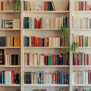 May include: A bright bookshelf displaying a variety of books. The books are arranged on white shelves, with different colours and sizes. Decorative plants and framed artwork enhance the display. A comfortable and welcoming home library.