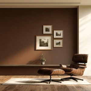 Könnte beinhalten: Ein brauner Loungesessel mit passendem Hocker, platziert auf einem hellen Teppich in einem Raum mit dunkelbraunen Wänden. An der Wand befinden sich vier gerahmte Bilder in einer Anordnung sowie ein schmales Regal mit einer kleinen Topfpflanze.