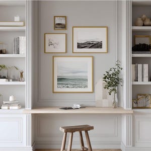 May include: A built-in white bookshelf with a desk and a small wooden stool. The shelves are filled with books, decorative items, and framed artwork. The artwork includes landscape and floral prints in gold frames.