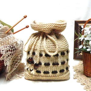 Könnte beinhalten: Eine beige gestrickte Kordeltasche mit braunen Punkten. Die Tasche liegt auf einem Tisch mit anderen Strickutensilien.