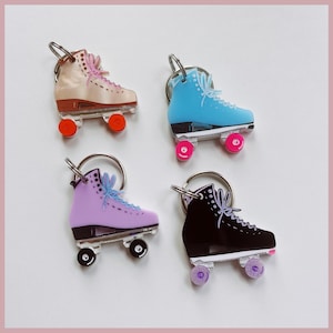 May include: Four roller skate keyrings in different colours: beige, light blue, lavender, and black. Each keyring features a silver key ring and a roller skate with white wheels and colourful accents.