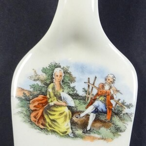 Może przedstawiać: Biały ceramiczny podkładka pod łyżkę z pozłacanym wykończeniem i malowanym obrazkiem przedstawiającym dwie osoby w ogrodzie. Podkładka pod łyżkę ma kwiatowy wzór na spodzie.