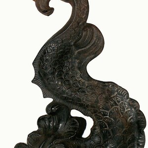 Puede incluir: Una escultura decorativa de hierro fundido negro que representa un pez estilizado con detalles intrincados. El pez está enroscado en forma circular con la cola levantada en alto.