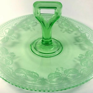 Può includere: Un vassoio da portata in vetro verde con manico. Il vassoio ha un design inciso con motivi paisley attorno al bordo.