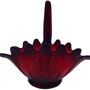 May include: A red glass basket with a herringbone pattern and a single handle. The basket is made of clear glass with a red tint.