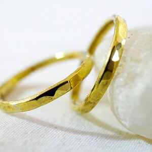 May include: Two gold-colored hammered metal rings, one slightly larger than the other, are stacked on top of each other. The rings are resting on a white surface.