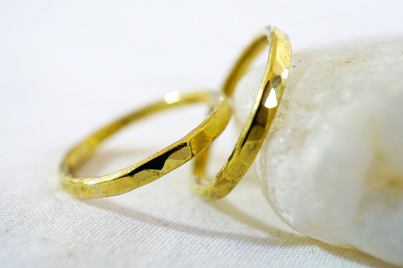 May include: Two gold-colored hammered metal rings, one slightly larger than the other, are stacked on top of each other. The rings are resting on a white surface.