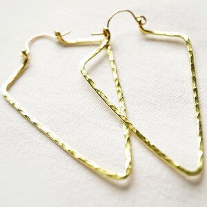 Puede incluir: Un par de pendientes geométricos dorados. Los pendientes tienen una textura martillada y una forma angular única. Se muestran sobre un fondo blanco, resaltando su brillo metálico. Estos pendientes son un accesorio elegante.