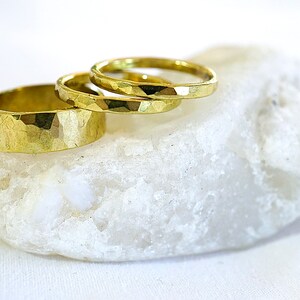 May include: Three gold hammered rings stacked on a white rock. The rings are different sizes and have a textured surface.