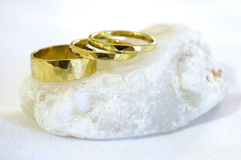 May include: Three gold hammered rings stacked on a white rock. The rings are different sizes and have a textured surface.