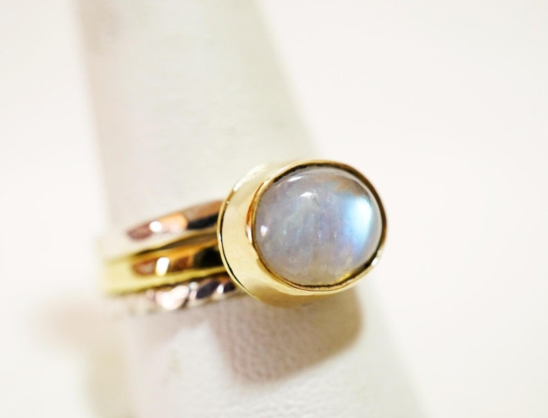 May include: A silver and gold ring with a white moonstone gemstone. The ring has a simple design and is set in a bezel setting.