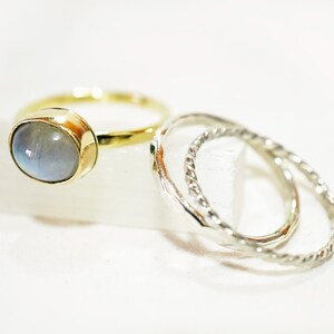 May include: A set of three rings, one with a light blue oval gemstone and two silver rings with a twisted design.