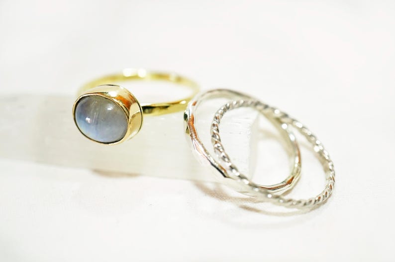 May include: A set of three rings, one with a light blue oval gemstone and two silver rings with a twisted design.
