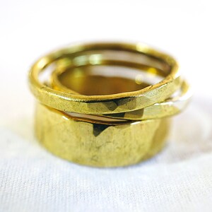 May include: Three gold rings stacked on top of each other. The top ring is smooth, the middle ring is textured, and the bottom ring is smooth.