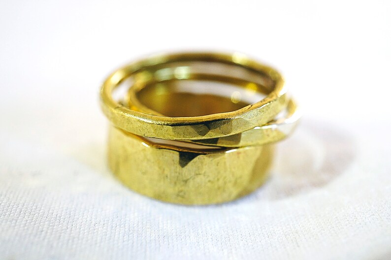 May include: Three gold rings stacked on top of each other. The top ring is smooth, the middle ring is textured, and the bottom ring is smooth.
