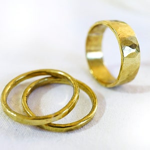 May include: Three gold rings, two are stacked on top of each other, and the third is lying flat on a white surface.
