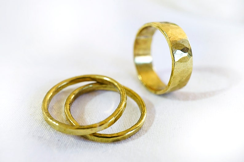 May include: Three gold rings, two are stacked on top of each other, and the third is lying flat on a white surface.