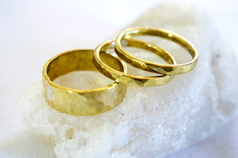 May include: Three gold hammered metal rings stacked on top of each other. The rings are all different sizes and have a textured surface.