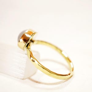May include: A gold ring with a white gemstone set in a bezel setting. The ring band is hammered and has a textured finish.