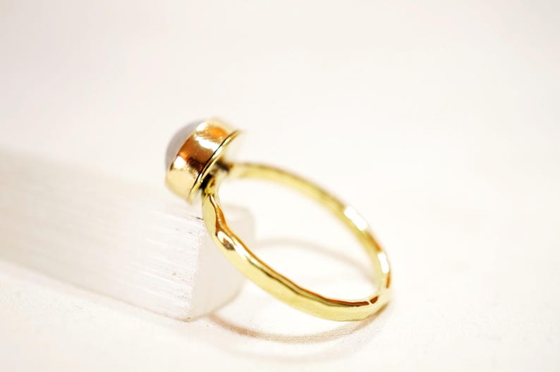 May include: A gold ring with a white gemstone set in a bezel setting. The ring band is hammered and has a textured finish.