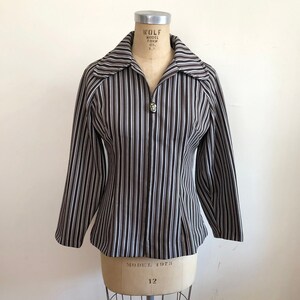May include: A brown and white striped jacket with a zipper closure and a collar. The jacket is on a dress form.