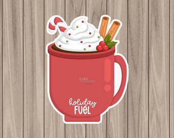 May include: A red mug of hot chocolate, decorated with whipped cream, a candy cane, cinnamon sticks, and berries. The mug has the words "holiday FUEL". The image is a sticker on a wood grain background.