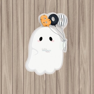 May include: A white ghost-shaped design with black eyes and rosy cheeks, holding three balloons. The balloons are orange with black stars, black with a white outline, and gray and white striped. The design is on a wooden background.