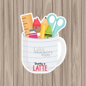 May include: A white mug-shaped sticker with school supplies, including a ruler, pencil, crayon, and scissors. The mug has blue lines and the text "thanks a LATTE". The background is a wooden surface.