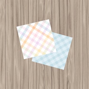 May include: Two square papers with a plaid pattern. One paper features a pastel plaid in pink, orange, yellow, and purple. The other has a light blue plaid. The papers are on a wooden surface.