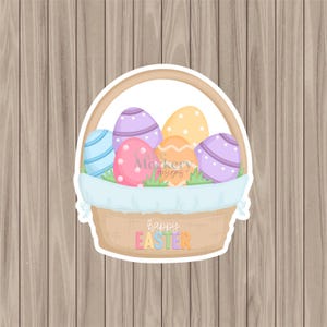 May include: A wicker basket filled with decorated Easter eggs. The eggs are painted with stripes, spots, and patterns in blue, pink, purple, and orange. The basket has a handle and the words "happy EASTER" are written on the front.