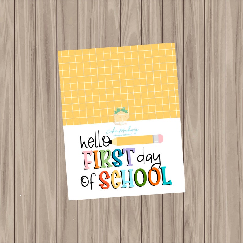 以下が含まれることがあります： 上部に黄色の格子模様があり、カラフルな文字で「hello FIRST day of SCHOOL」と書かれた長方形のカード。黄色の鉛筆のグラフィックが含まれています。カードは木製の表面にあります。