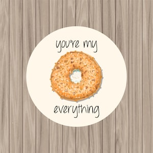 May include: A white circle with the text "you're my everything" and a drawing of a bagel with cream cheese on a wood background.
