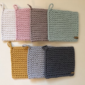 May include: Set of 8 knitted pot holders in various colors, including white, pink, gray, green, yellow, and blue. The pot holders are square shaped and have a woven texture.