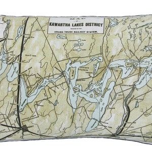 May include: Rectangular cushion displaying a vintage map of the Kawartha Lakes District, with text indicating the Grand Trunk Railway System. The map is in beige, green, and blue, with black lines and text. The cushion has a white border.