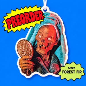 May include: A die-cut air freshener featuring a graphic of a creature with a towel wrapped around its head, holding a gold hand mirror. The text PREORDER appears in a yellow starburst, and the text SCENT: FOREST FIR appears in a green starburst.