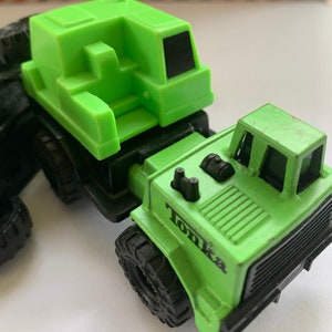 May include: Green Tonka toy truck with a green crane attachment. The truck has black tires and a black grill. The crane has a black cab.