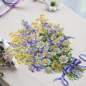May include: A cross-stitch embroidery of a bouquet of purple and white flowers with a blue ribbon and the text "2021" in the bottom right corner.