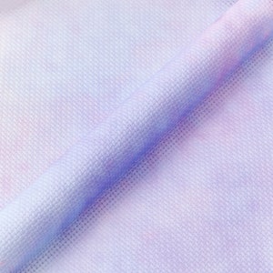 May include: Close-up of a soft, textured fabric with a tie-dye pattern in shades of purple, pink, and white.