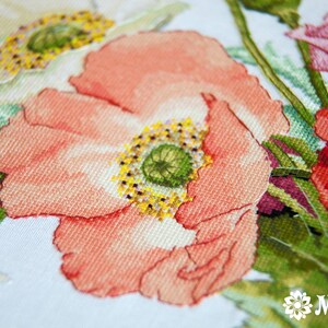May include: Close-up of a cross-stitch embroidery featuring a bouquet of pink, red, and white poppies with green leaves and a bee.