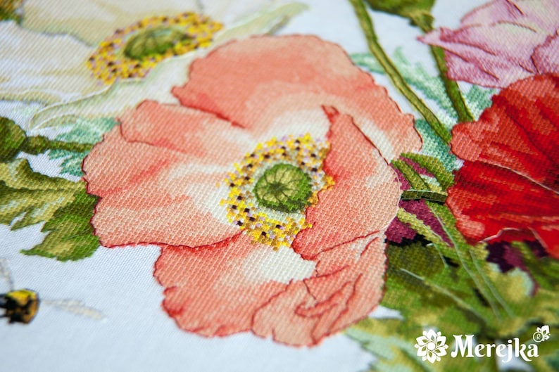 May include: Close-up of a cross-stitch embroidery featuring a bouquet of pink, red, and white poppies with green leaves and a bee.
