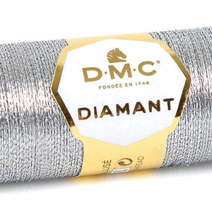 K&ouml;nnte beinhalten: Eine silberne Metallic-Garnrolle mit der Aufschrift "D.M.C. Fond&eacute;e en 1746 Diamant"