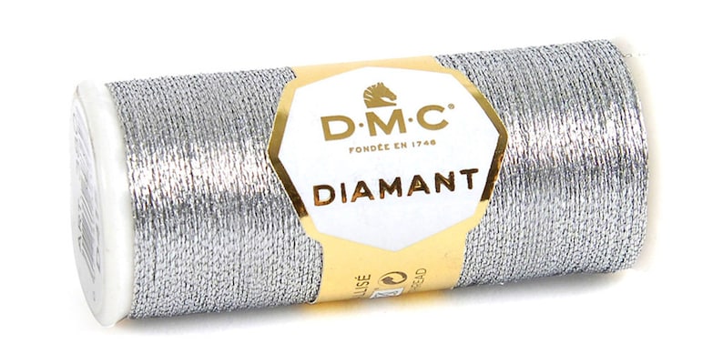 K&ouml;nnte beinhalten: Eine silberne Metallic-Garnrolle mit der Aufschrift "D.M.C. Fond&eacute;e en 1746 Diamant"