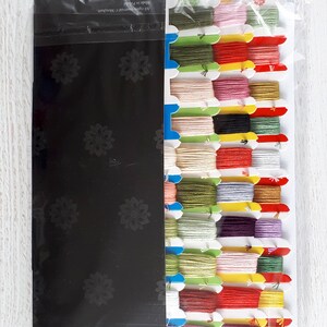 May include: A set of embroidery floss in a variety of colors, including red, green, yellow, pink, and purple. The floss is organized in a plastic container with a black background. The text "All rights reserved c. Marigolds" and "Made in Taiwan" is printed on the container.