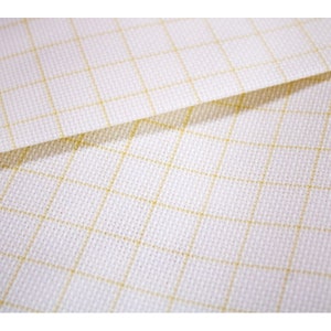May include: White Aida cloth with a grid pattern in a light yellow color. The cloth is folded in half, showing the grid pattern on both sides.