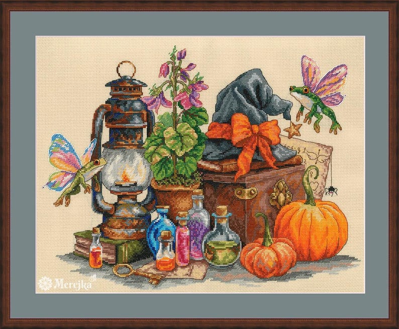 May include: A cross-stitch pattern featuring a dark lantern, a potted purple flower, a black hat with an orange bow, two pumpkins, and glass potion bottles. Two green frogs with colorful wings are present, along with a key and a small spider.