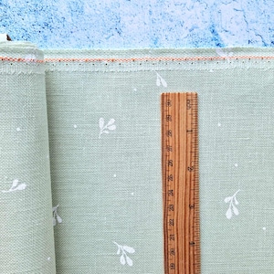 Può includere: Un tessuto verde pallido con un motivo floreale bianco e un righello che misura 7,6 cm. Il tessuto ha una texture sottile e una sensazione leggera e ariosa.