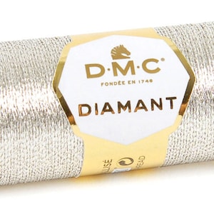K&ouml;nnte beinhalten: Eine silberne Metallic-Garnrolle mit der Aufschrift "DMC Diamant", dem DMC-Logo und dem Text "Fond&eacute;e en 1746".