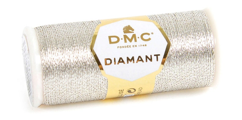 K&ouml;nnte beinhalten: Eine silberne Metallic-Garnrolle mit der Aufschrift "DMC Diamant", dem DMC-Logo und dem Text "Fond&eacute;e en 1746".