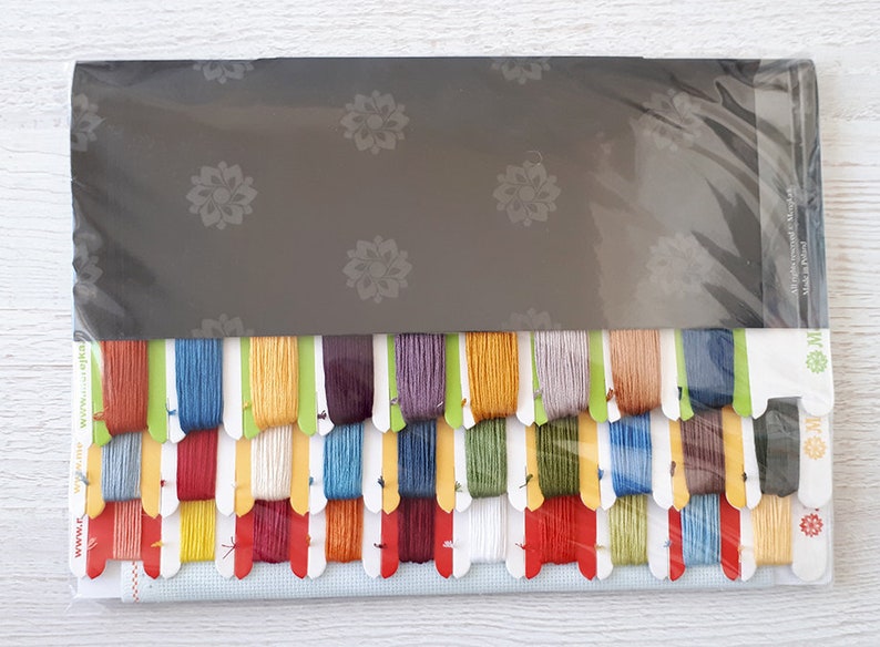 Puede incluir: Un kit de punto de cruz con una variedad de hilos de colores, un trozo de tela Aida y instrucciones. El kit est&aacute; empaquetado en una bolsa de pl&aacute;stico transparente con un respaldo negro.