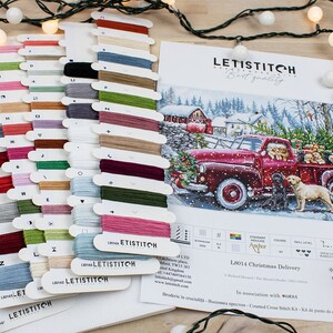 May include: A cross stitch kit featuring a red truck with a Christmas tree and dogs in the back. The kit includes a variety of colored threads and a pattern for the design. The kit is titled "L8014 Christmas Delivery".